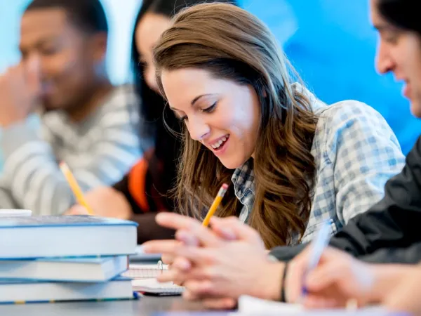 Smiling young people sitting at a table with books and pencils.