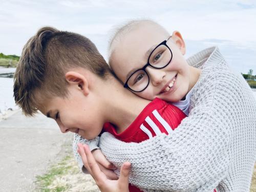 Two children are hugging: a little boy in a red football top and a young girl with short hair.