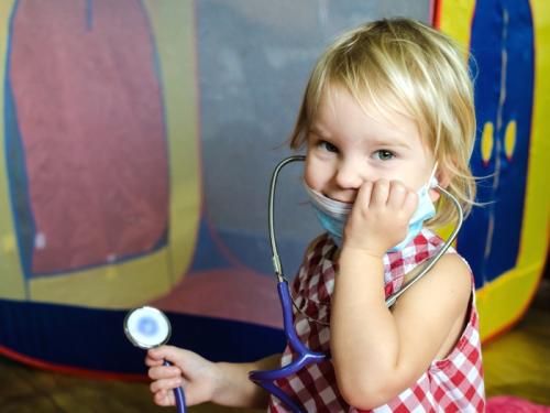 A young girl playing with a stethescope and smiling at the camera