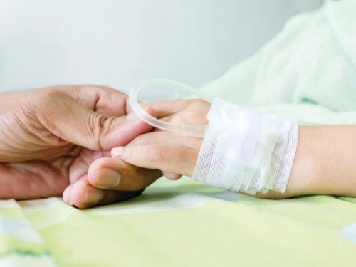 A child's hand with an IV drip holding an adult's hand