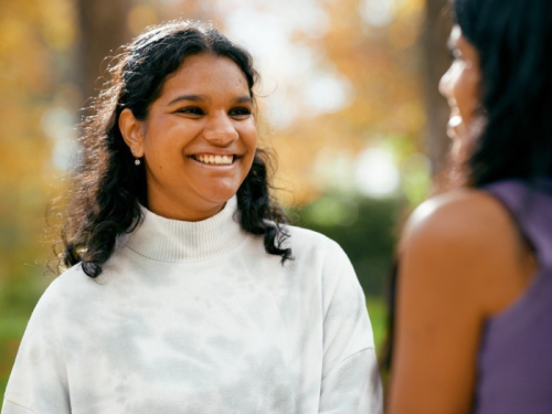Indian girl with white blouse and shoulder length black hair smiling and talking to another Indian girl 
