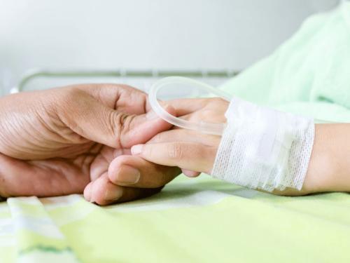 An adult hand holding a child's hand which has an IV tube and bandages