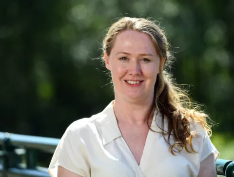 A professional woman with brown hair and a cream v neck top 
