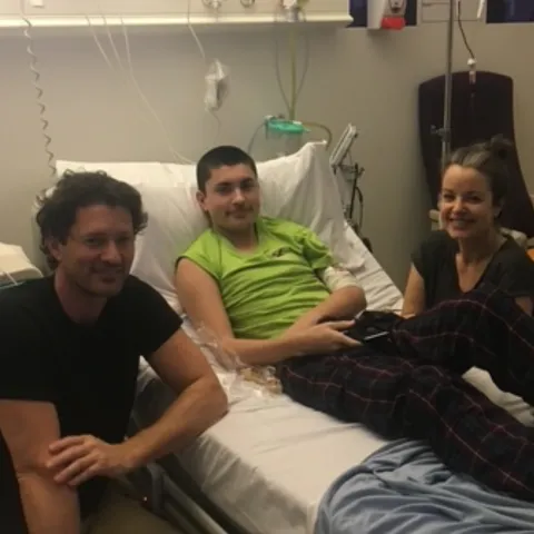 Dad, mum and son sitting in a cancer warn on a hospital bed 