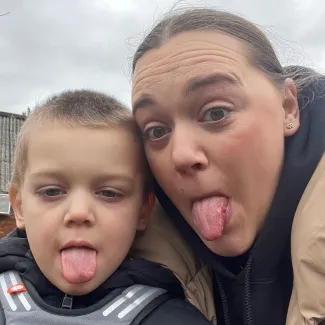 A woman and her son are close together, both sticking their tongues out for the camera.