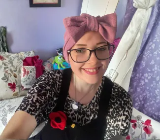 A young woman is taking a selfie, she is smiling and wearing a headband with a large pink bow.