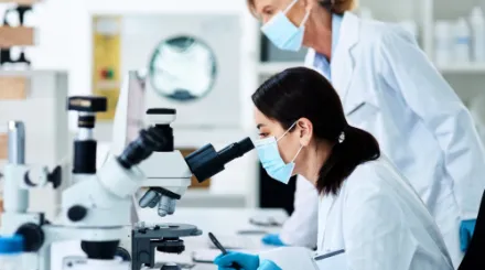 Two female researchers in lab coats using microscopes.
