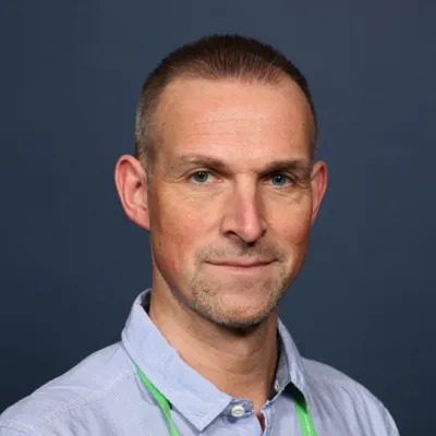 Professor Gareth Veal with short hair, wearing a light blue shirt and smiling at the camera.