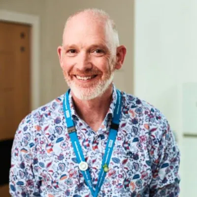 Rob smiling at the camera wearing a floral shirt and blue lanyard.