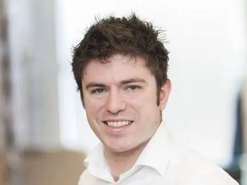 Johnathan smiling at the camera. He has dark hair and is wearing a white shirt.
