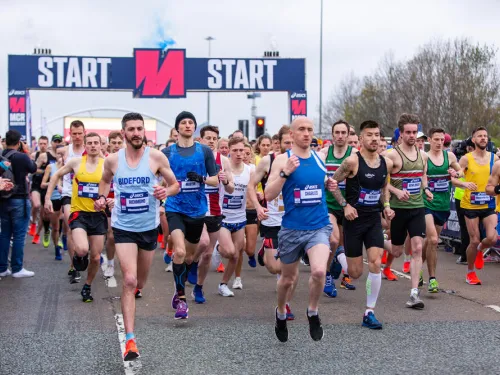 A large group of runners going past the starting line of the Manchester Marathon.