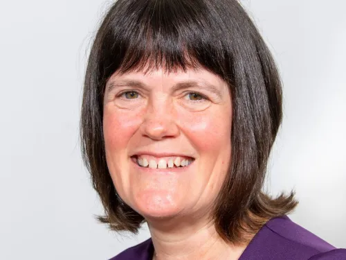 Chris smiling at the camera with short dark hair and wearing a purple top.