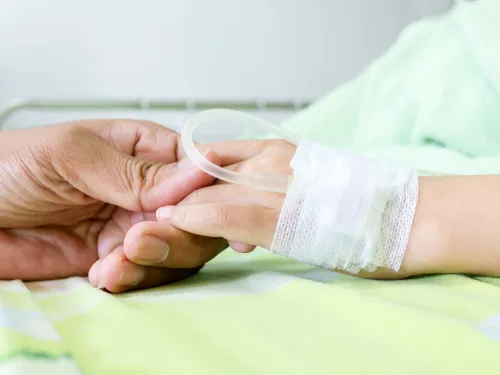 A child's hand, bandaged with a drip, holding an adult's hand.