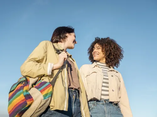 A young couple smiling at each other against a blue sky.