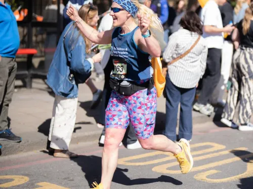 A woman running a marathon, smiling and holding her fists in the air as she runs past other people