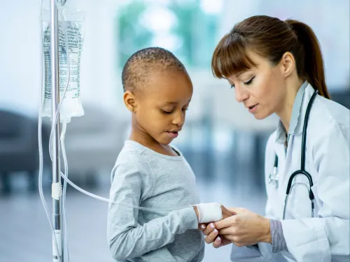 A child with a drip stand talking to a doctor in a white lab coat.