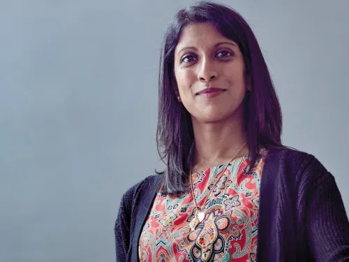 Shaarna smiling at the camera with mid-length dark brown hair and wearing a colourful patterned blouse.