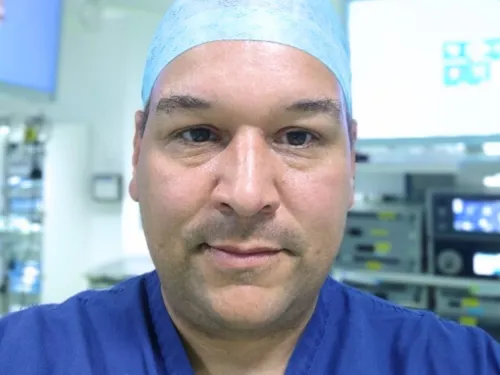 Mr Max Pachl smiling at the camera while wearing blue surgical scrubs and hat.