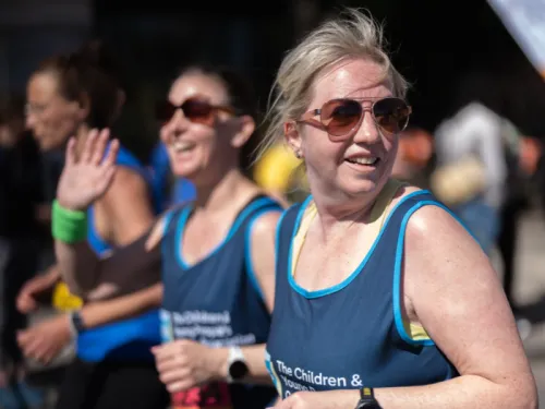 Two women running the London Landmarks half marathon, wearing CCLG tops, waving and smiling at the camera