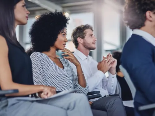 People sitting in a meeting, focused on an unseen speaker