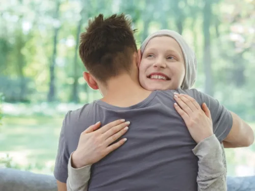 A young girl with a headscarf, smiling and hugging a young boy