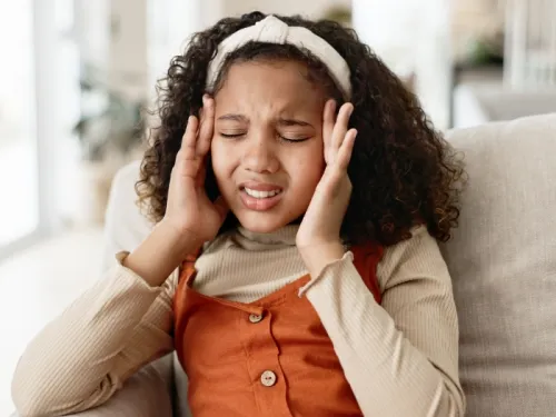 A young girl holding the sides of her head in pain