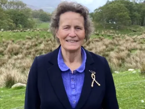 Kathy Pritchard-Jones stood outside, wearing a black blazer with a gold ribbon brooch.