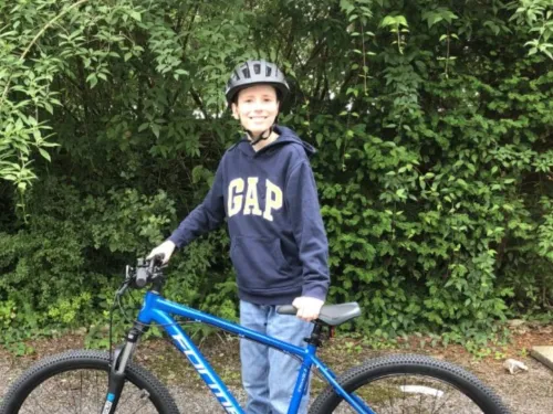 A boy wearing a bike helmet standing behind his blue two wheel bike