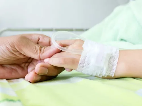 A male adult hand holding a child's hand that has an IV drip on a hospital bed
