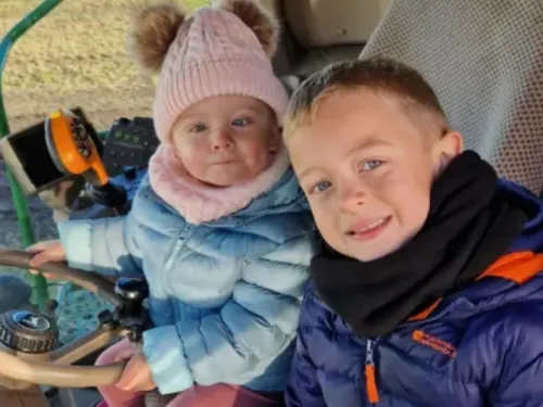 Little girl with blue coat and pink hat with retinoblastoma and her little brother